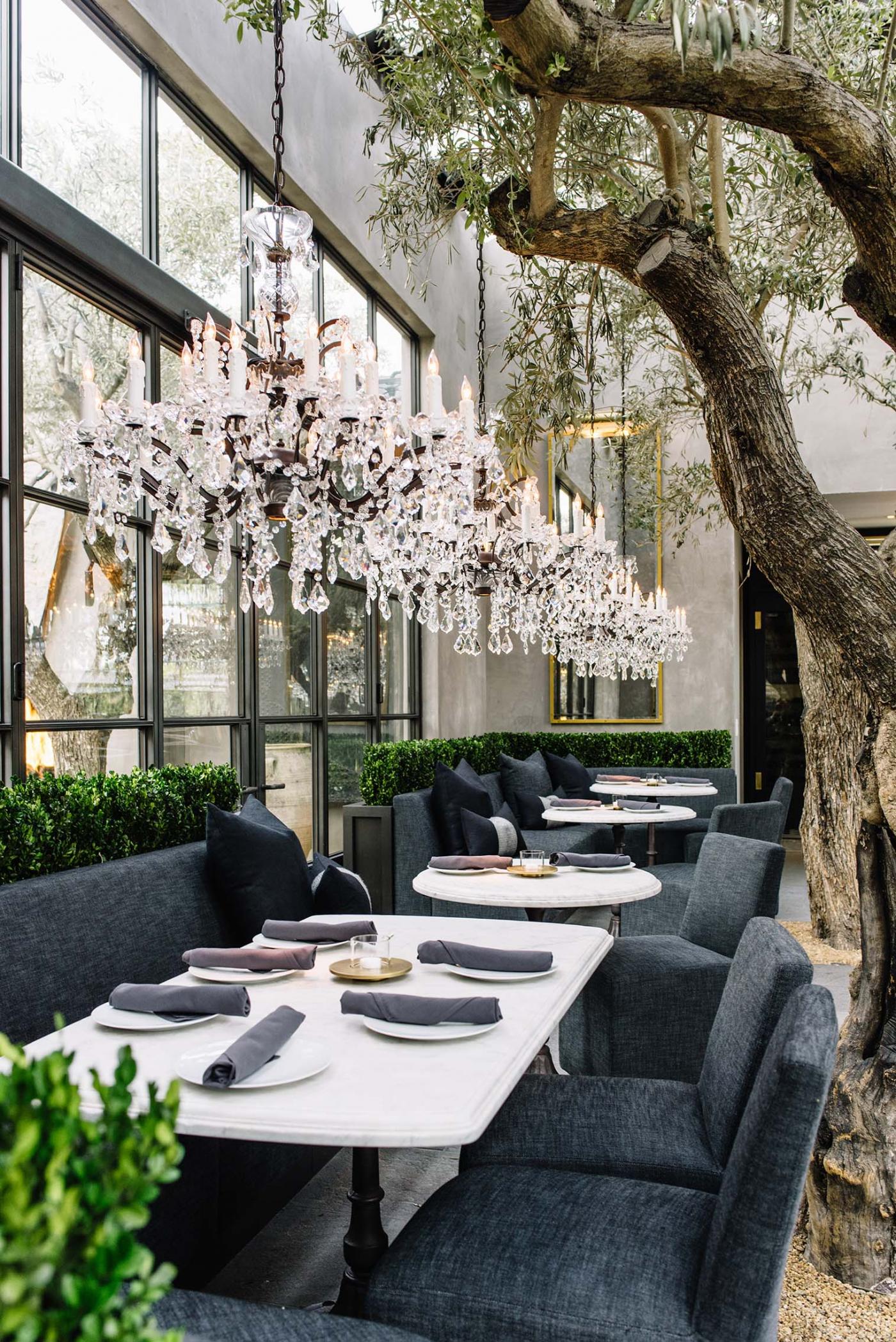 dining tables lined with table settings under chandeliers and trees