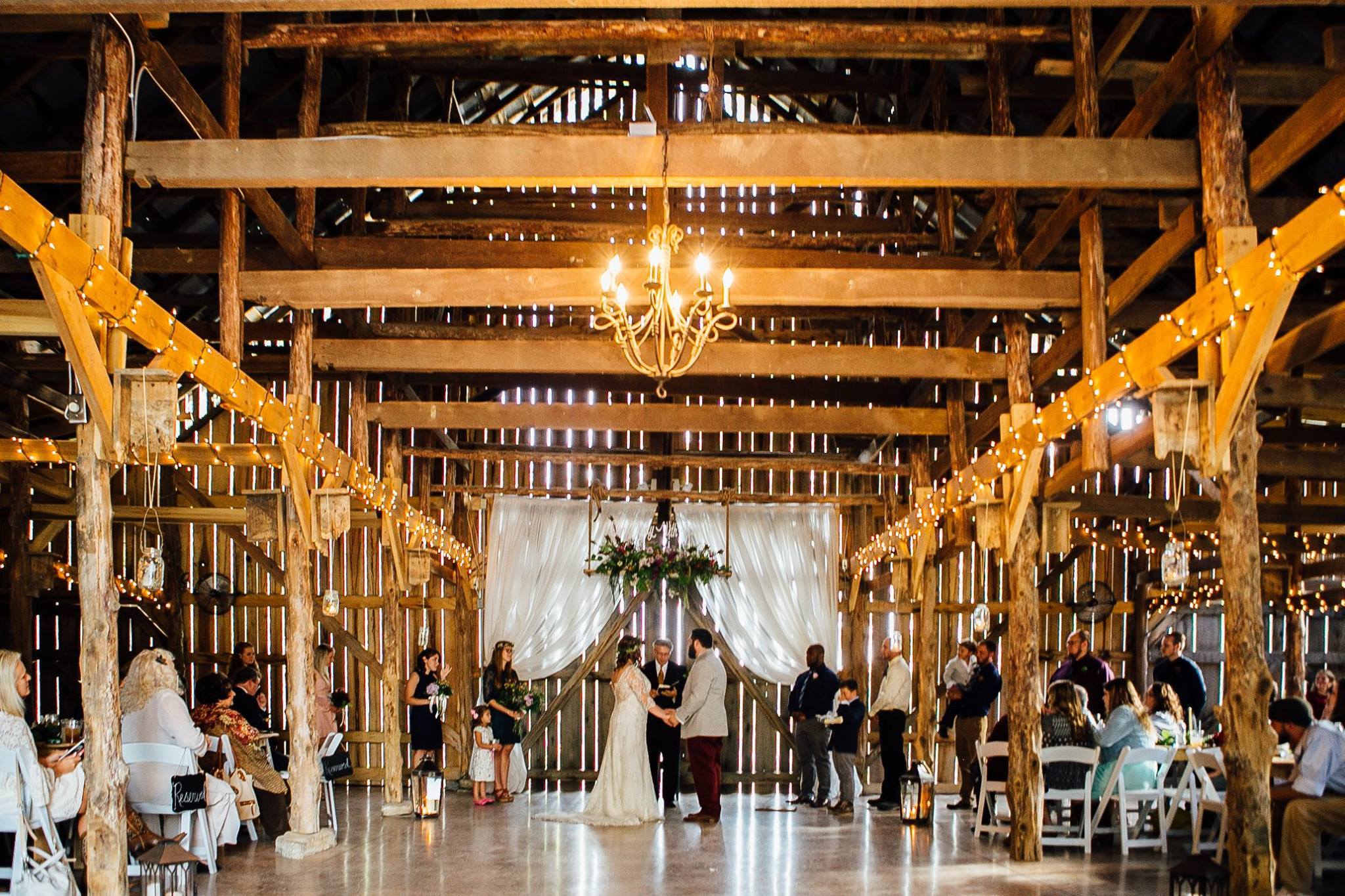 Barn Wedding Ceremony with hanging chandelier and exposed wood work.
